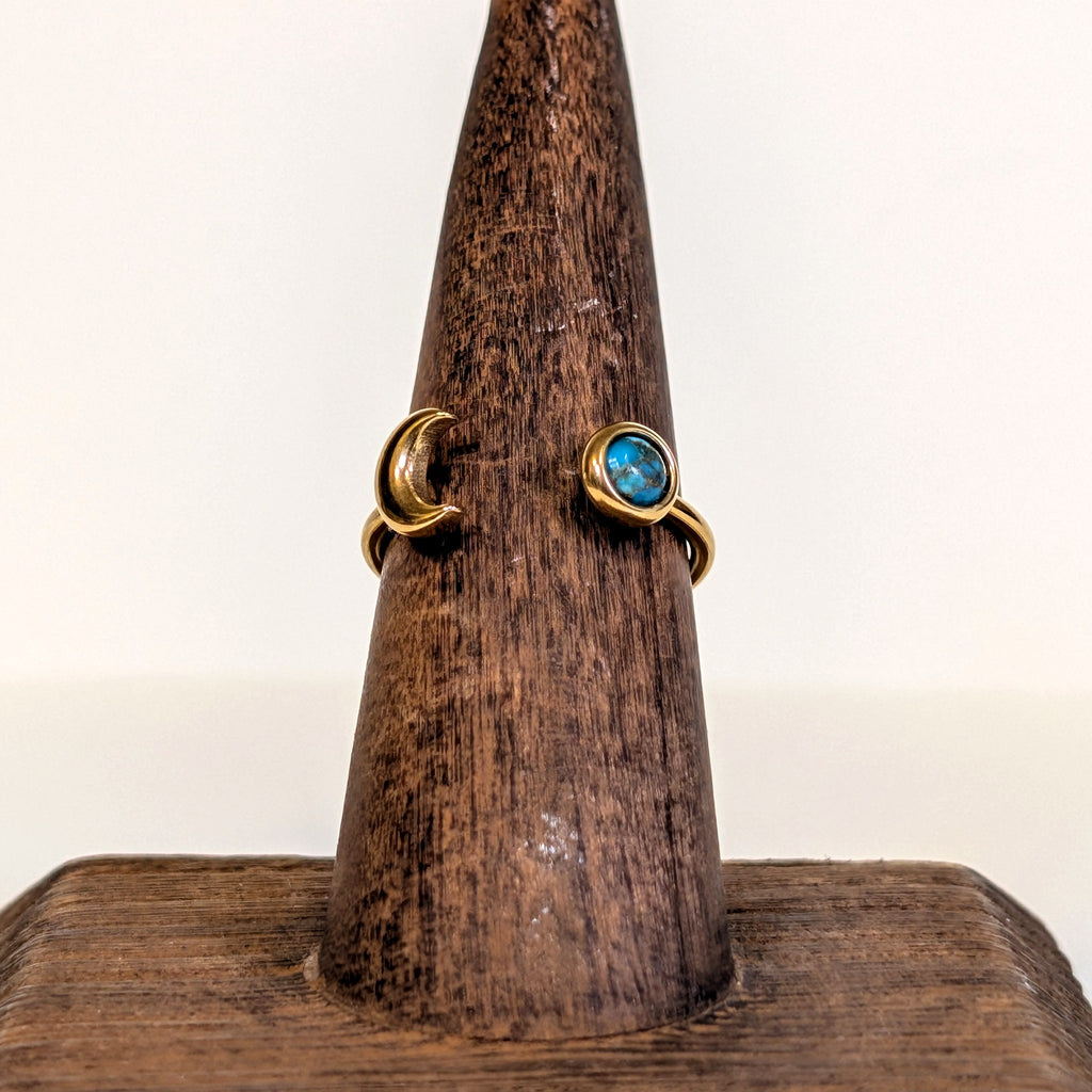 Eclipse Ring with a blue copper turquoise cabochon and a gold crescent moon, on a wooden ring stand