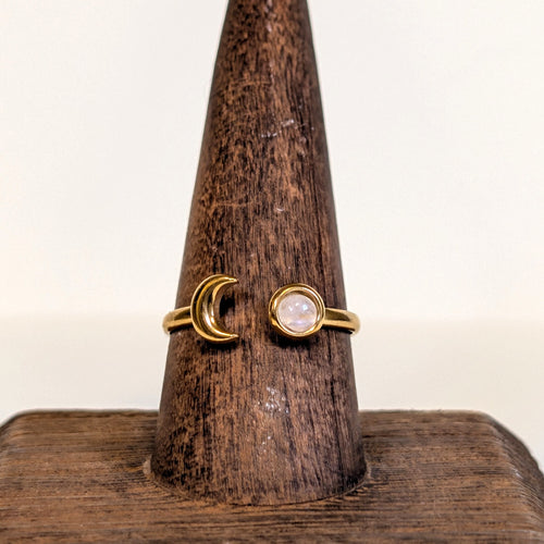 Eclipse Ring with a rainbow moonstone cabochon and a gold crescent moon, on a wooden ring stand