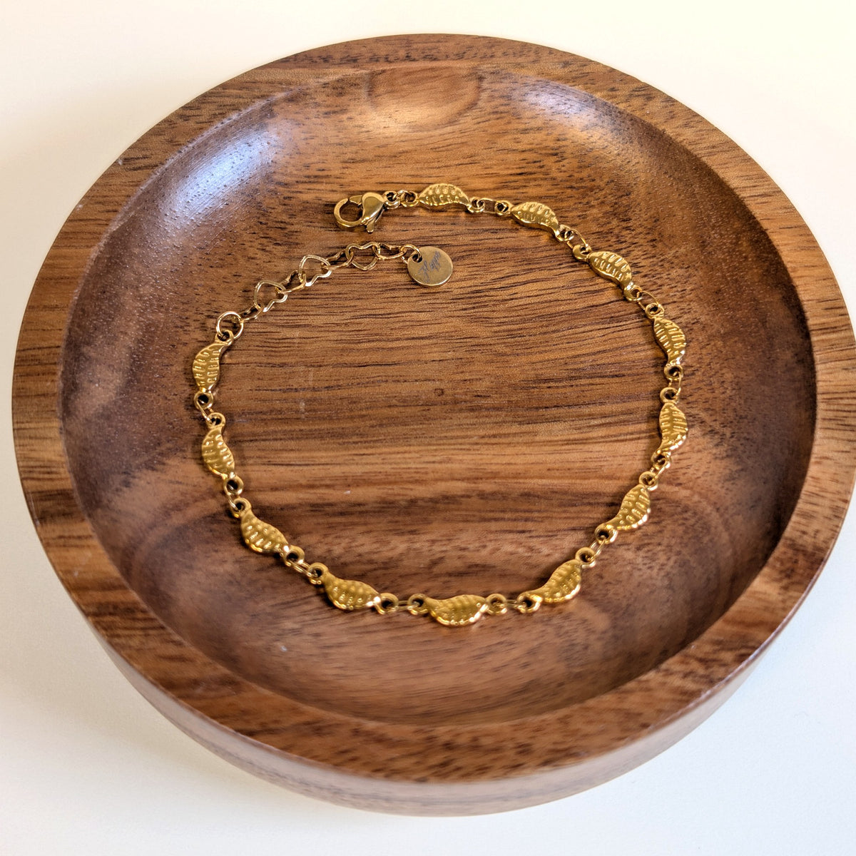 Falling Leaves gold bracelet with lobster clasp and heart-link extender, shown in a walnut dish