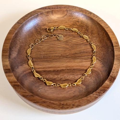 Falling Leaves gold bracelet with lobster clasp and heart-link extender, shown in a walnut dish