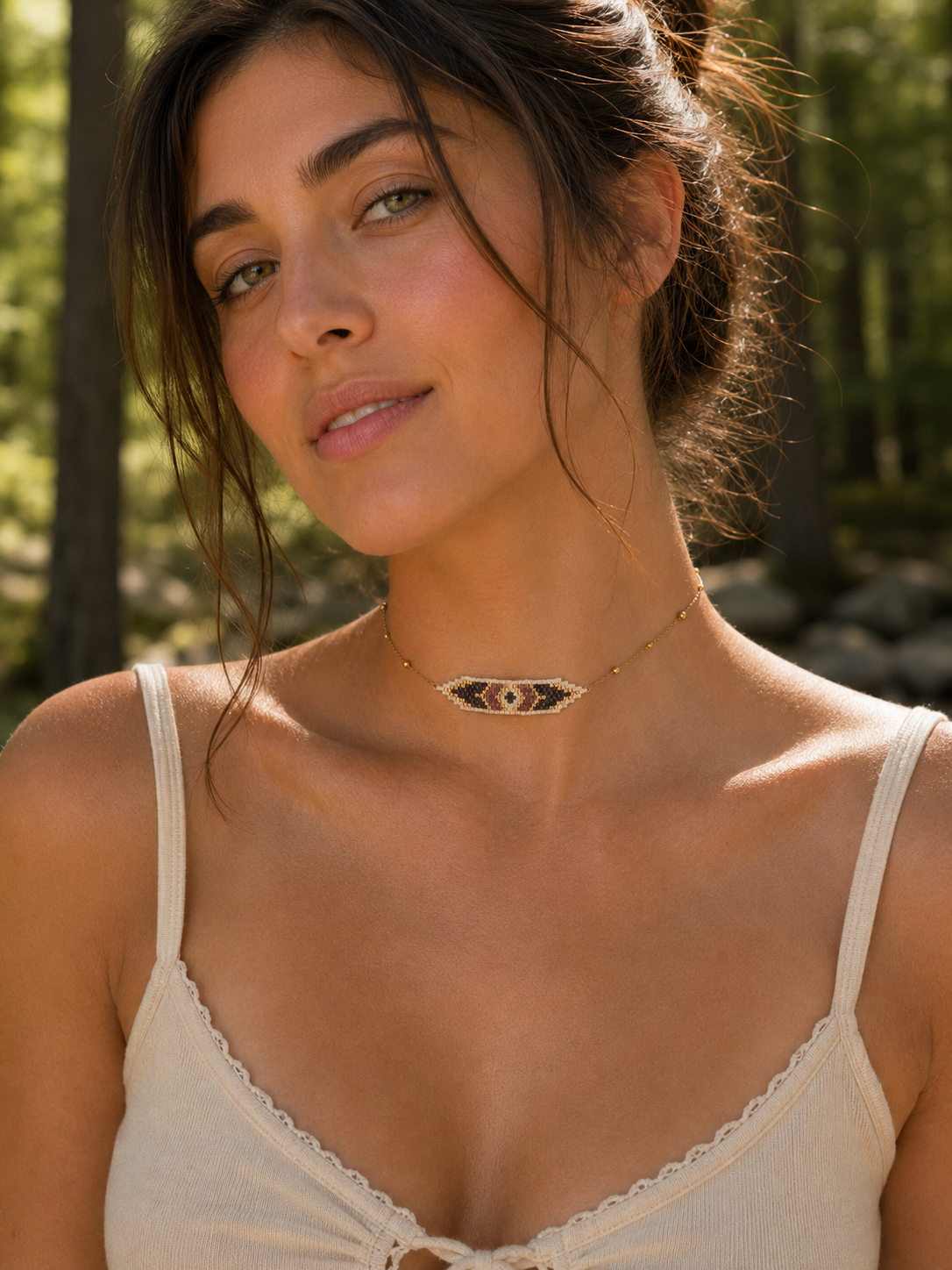 A woman outdoors wearing a delicate gold chain necklace with a geometric, chevron-like pattern in black, white, and red beads.