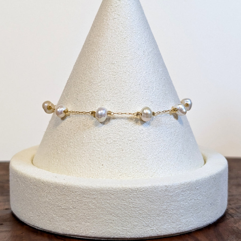 Floating Pearls bracelet with genuine freshwater pearls on a fine gold chain, shown on a display cone