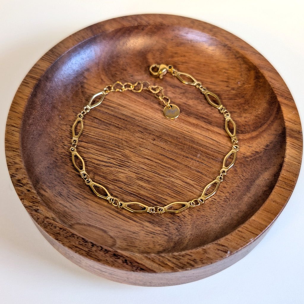 Golden Links gold bracelet with lobster clasp and heart-link extender, shown in a walnut dish
