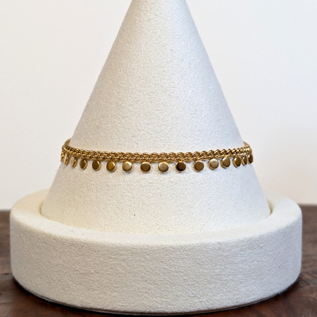 Golden Rain bracelet with small gold discs along a curb chain, shown on a display cone