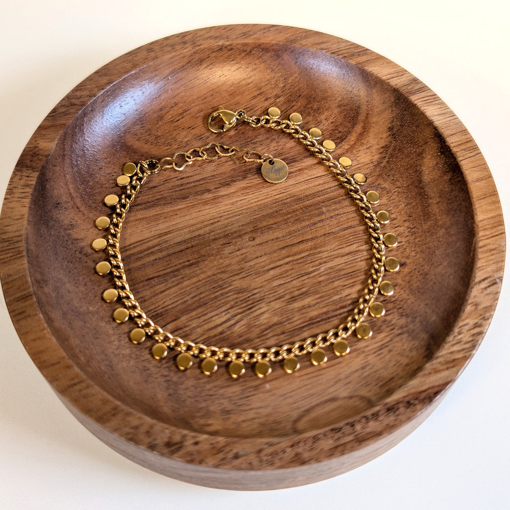 Golden Rain gold disc bracelet with lobster clasp and heart-link extender, shown in a walnut dish