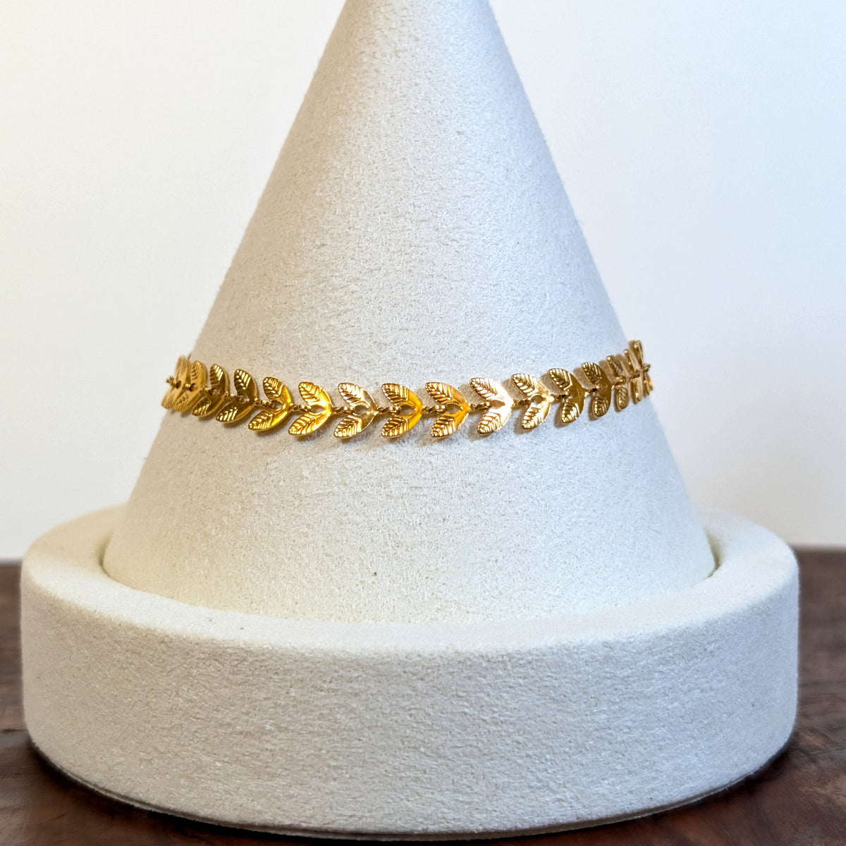 Golden Vine gold bracelet with a continuous laurel-leaf chain, shown on a display cone