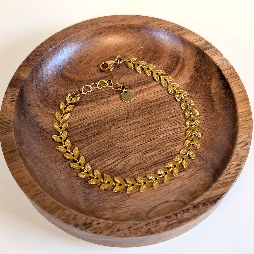 Golden Vine gold bracelet with lobster clasp and heart-link extender, shown in a walnut dish