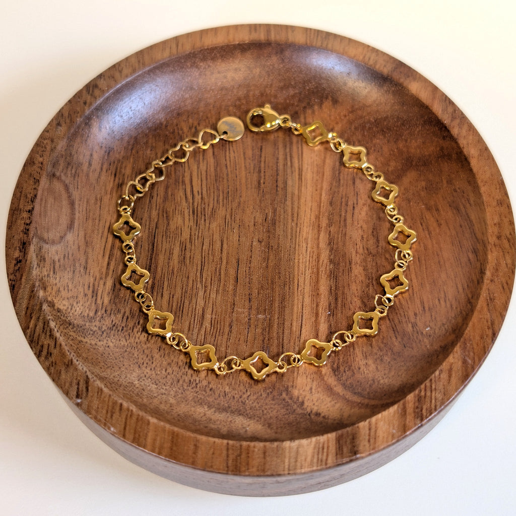 Lucky Clover gold bracelet with lobster clasp and heart-link extender, shown in a walnut dish