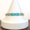 Handwoven Miyuki Delica bracelet in turquoise, gold and ivory on a display cone