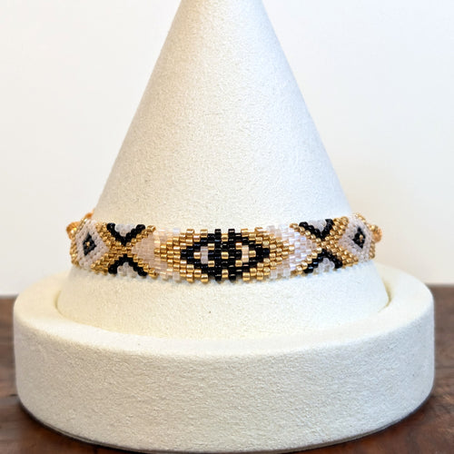 Handwoven Miyuki Delica bracelet in ivory, gold and black on a display cone