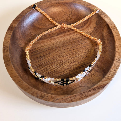 Woven Roots Ivory beaded bracelet with adjustable braided cord, shown in a walnut dish