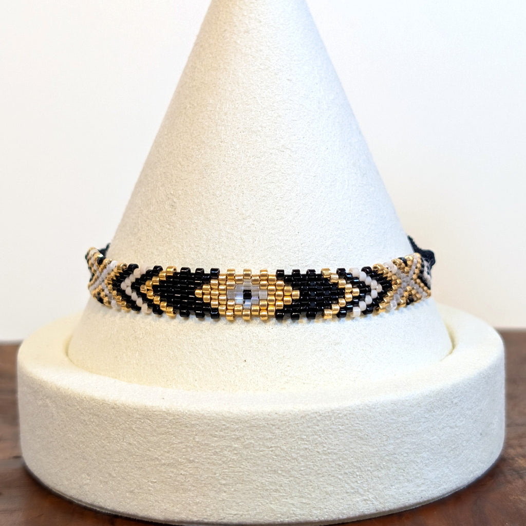 Handwoven Miyuki Delica bracelet in black, gold and ivory on a display cone
