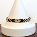 Handwoven Miyuki Delica bracelet in black, gold and ivory on a display cone