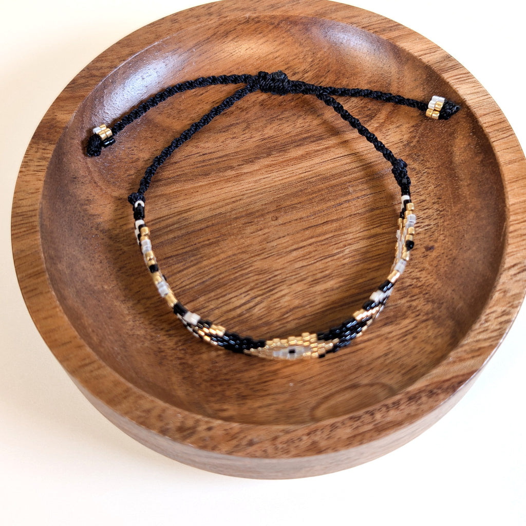 Woven Roots Onyx beaded bracelet with adjustable black cord, shown in a walnut dish