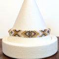 Handwoven Miyuki Delica bracelet in pearl white, gold and gunmetal grey on a display cone