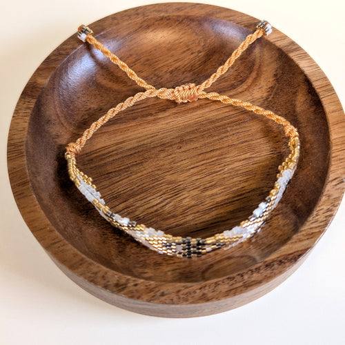 Woven Roots Pearl beaded bracelet with adjustable braided cord, shown in a walnut dish