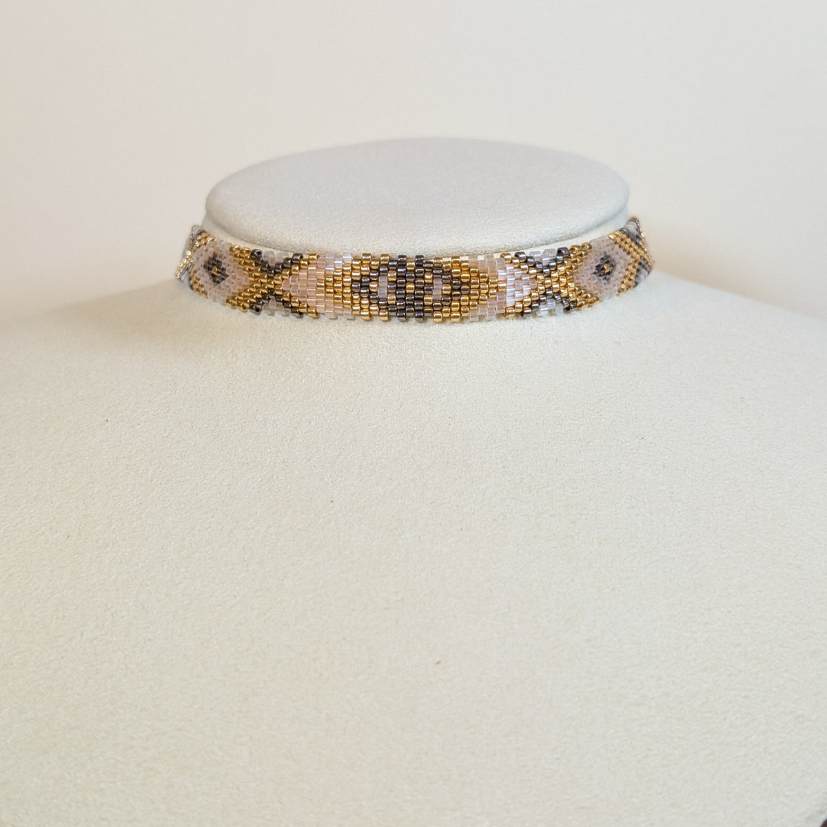 Wide Miyuki beaded choker band in gold, bone and grey with dark diamonds, on a white display bust