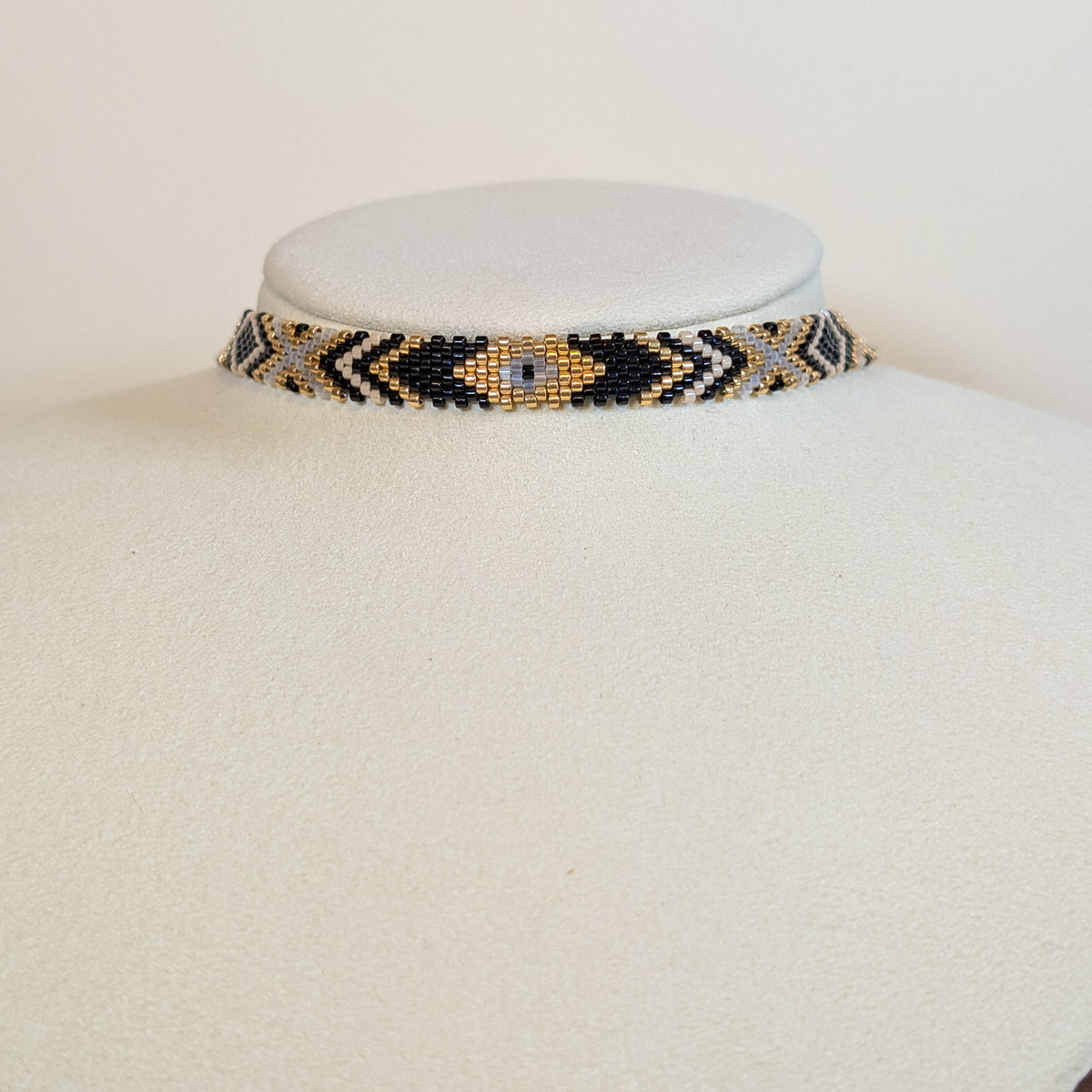 Wide Miyuki beaded choker band in black, gold, silver and grey arrow patterns, on a white display bust