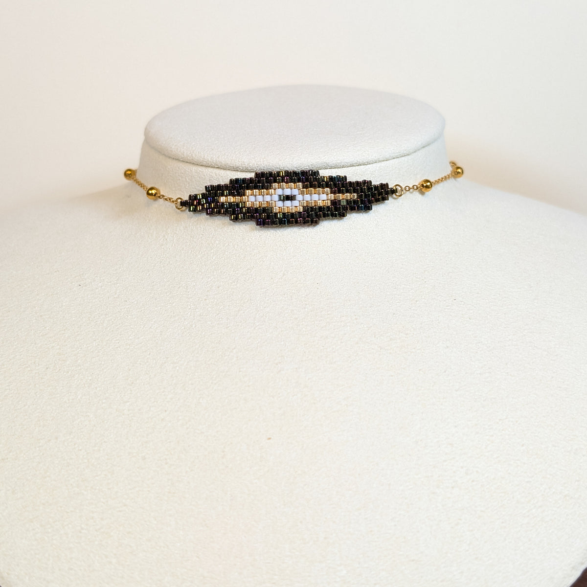 Miyuki beaded choker in black and gold with a pale eye at the centre, on a white display bust