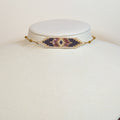 Miyuki beaded choker in plum, dusty rose and slate with a bone and gold border, on a white display bust