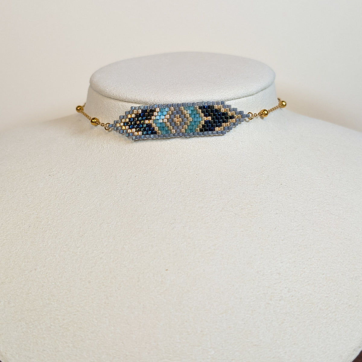 Miyuki beaded choker in slate blue, turquoise, gold and bone layered diamonds, on a white display bust