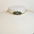 Miyuki beaded choker with a teal and gold diamond pattern on a white display bust