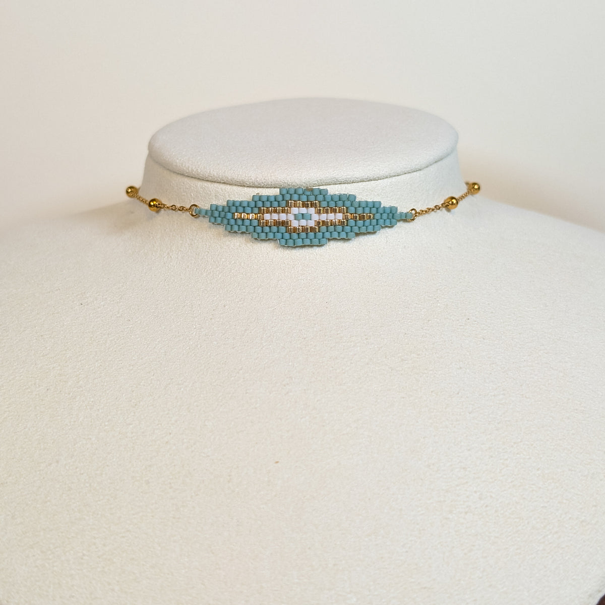 Miyuki beaded choker with a turquoise diamond and white centre bordered in gold, on a white display bust
