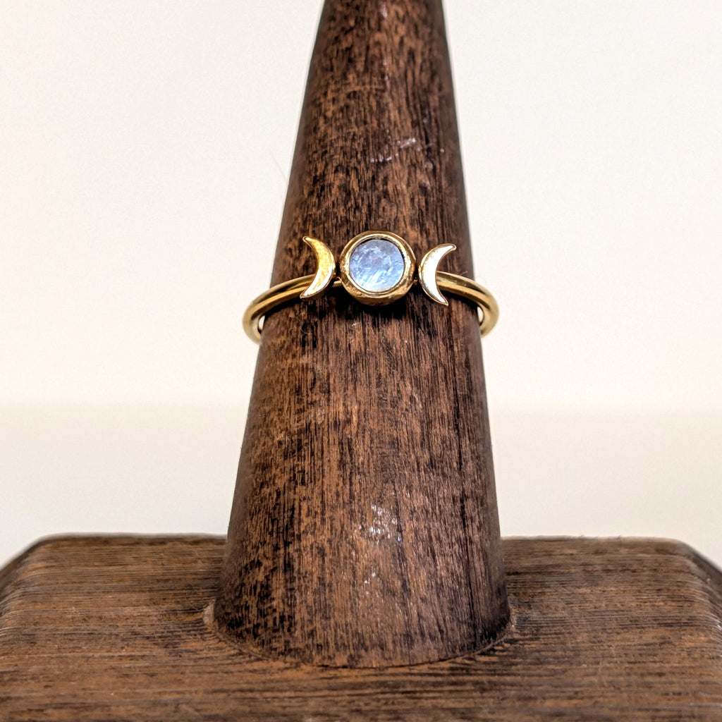 Moon Goddess Ring with a rainbow moonstone set between two gold crescent moons, on a wooden ring stand