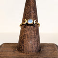 Moon Goddess Ring with a rainbow moonstone set between two gold crescent moons, on a wooden ring stand