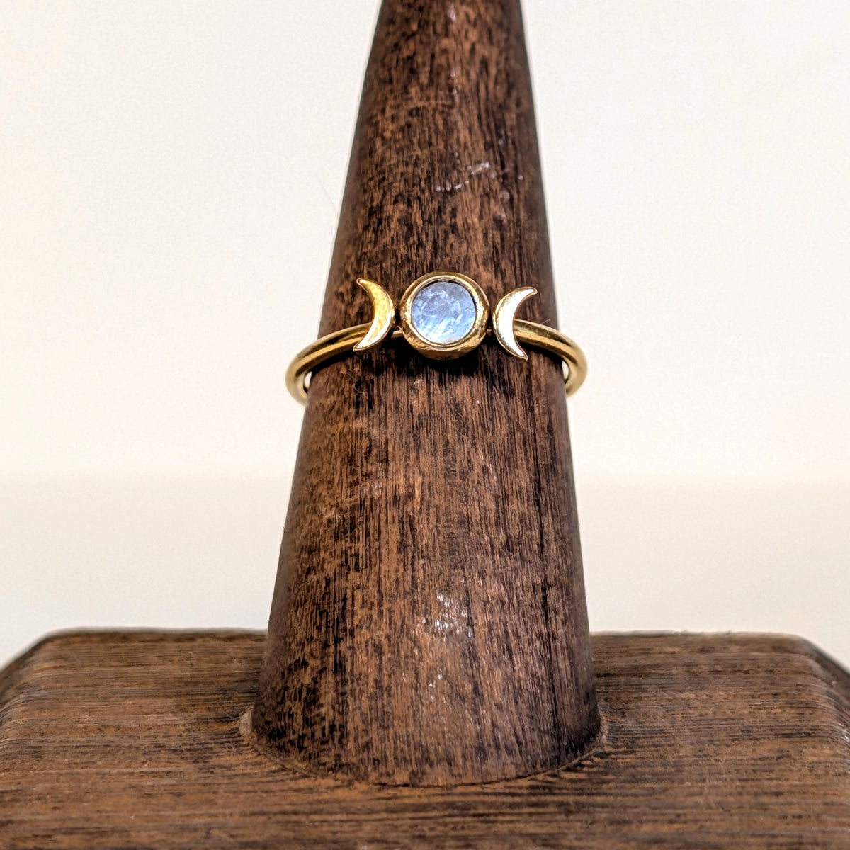 Moon Goddess Ring with a rainbow moonstone set between two gold crescent moons, on a wooden ring stand