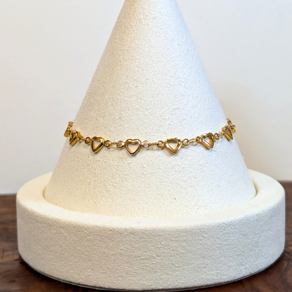 Open Hearts gold bracelet with a row of open heart links, shown on a display cone