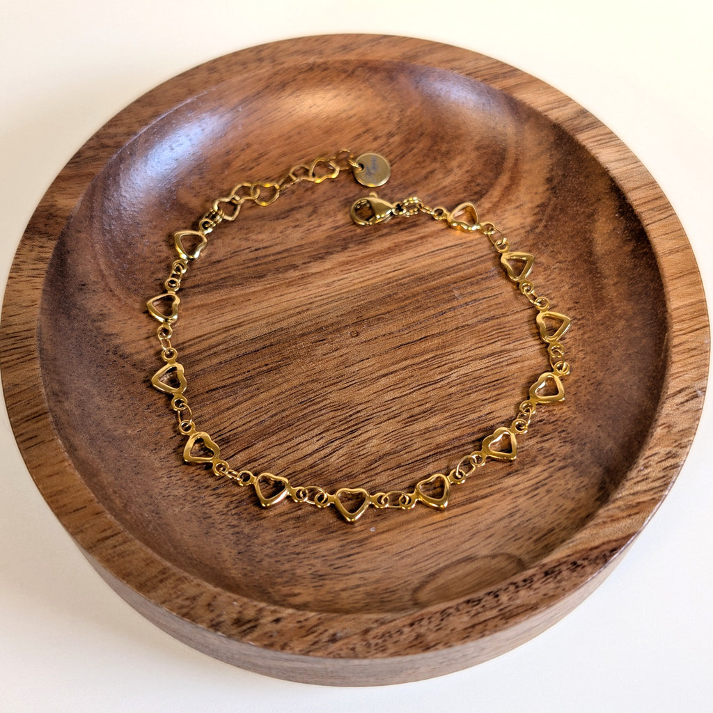 Open Hearts gold bracelet with lobster clasp and heart-link extender, shown in a walnut dish