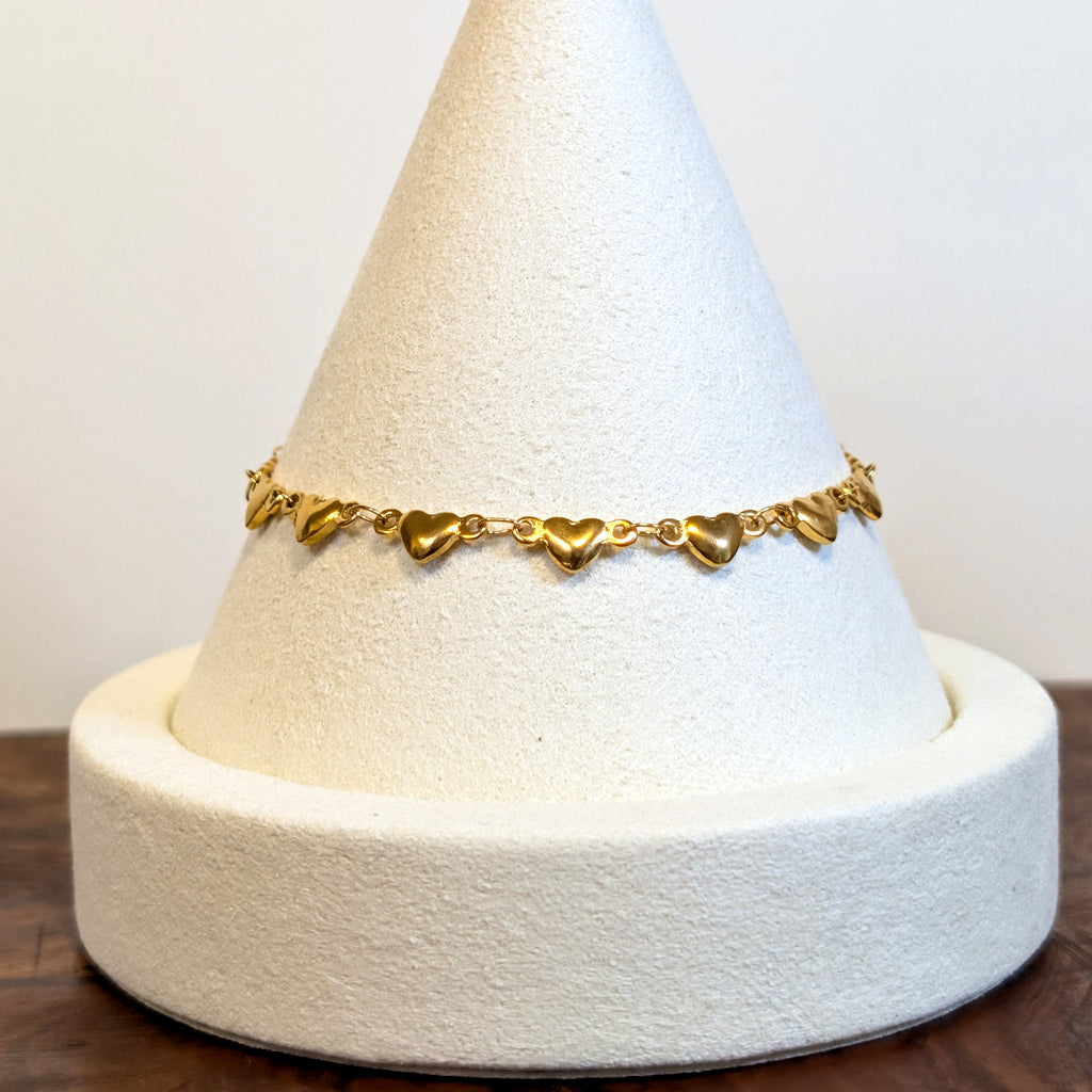 Puffy Heart gold bracelet with solid rounded heart links, shown on a display cone