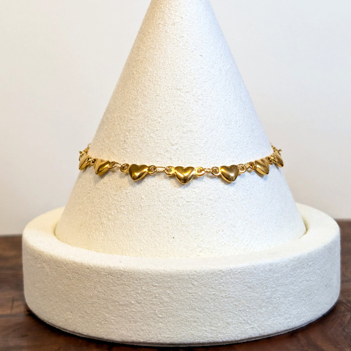Puffy Heart gold bracelet with solid rounded heart links, shown on a display cone