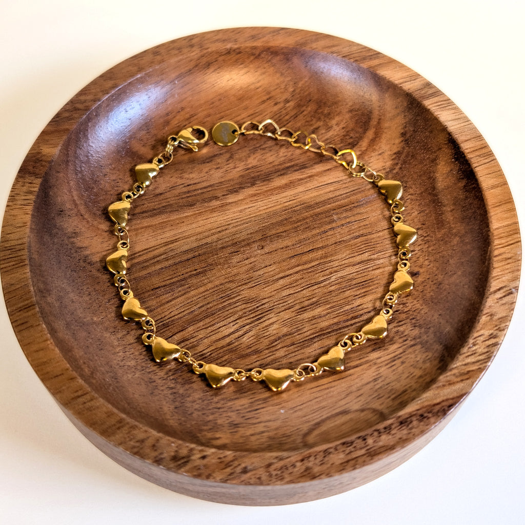 Puffy Heart gold bracelet with lobster clasp and heart-link extender, shown in a walnut dish