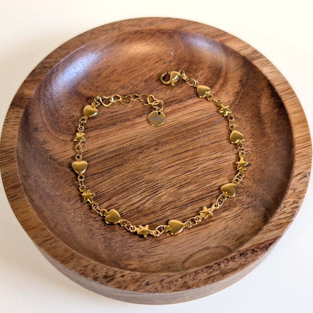 Starry Heart gold bracelet with lobster clasp and heart-link extender, shown in a walnut dish