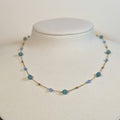 Gold-tone stainless steel fine chain choker with aqua and pale blue beads on a white display bust