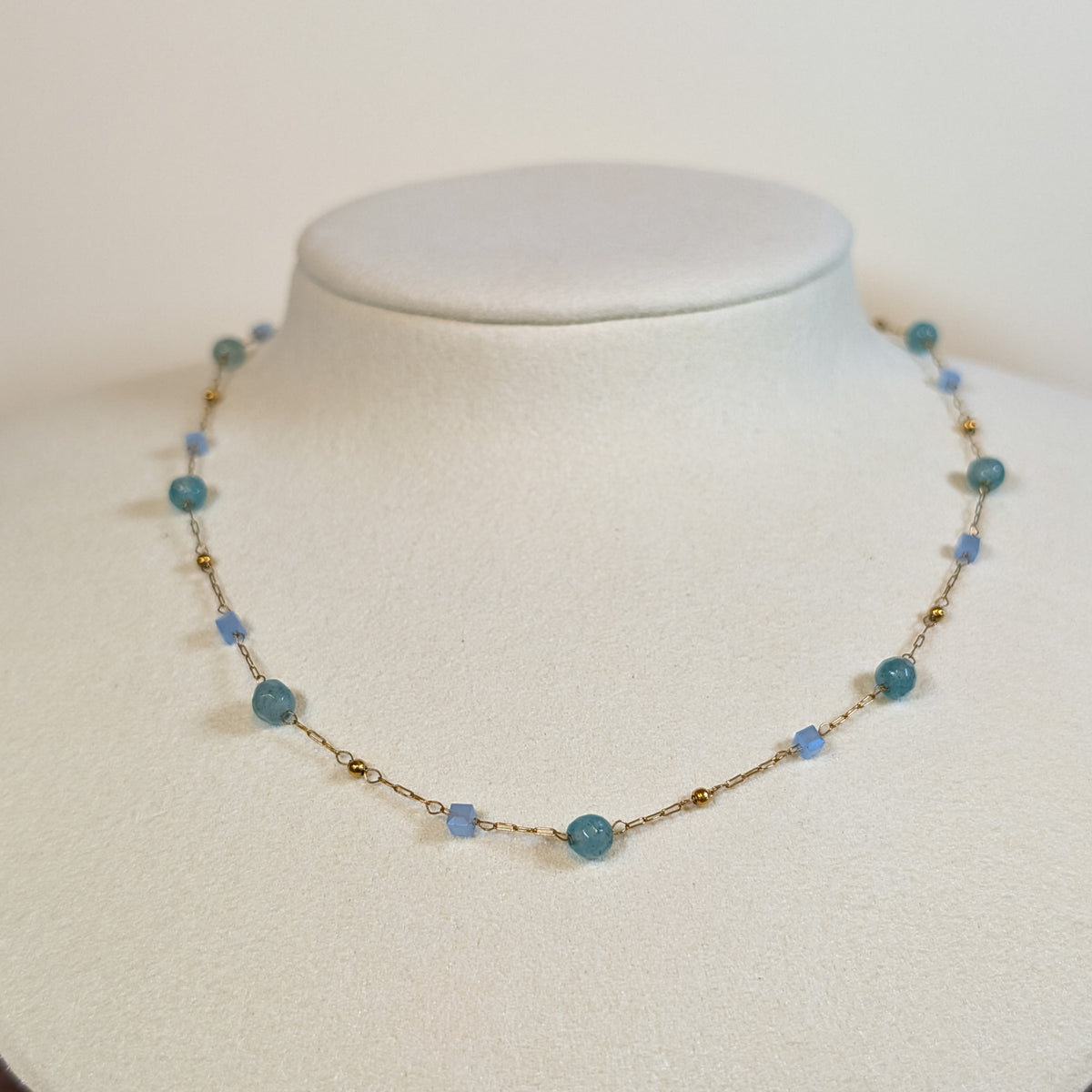 Gold-tone stainless steel fine chain choker with aqua and pale blue beads on a white display bust