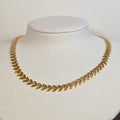 Gold-tone stainless steel choker chain woven in a laurel fishbone leaf pattern on a white display bust