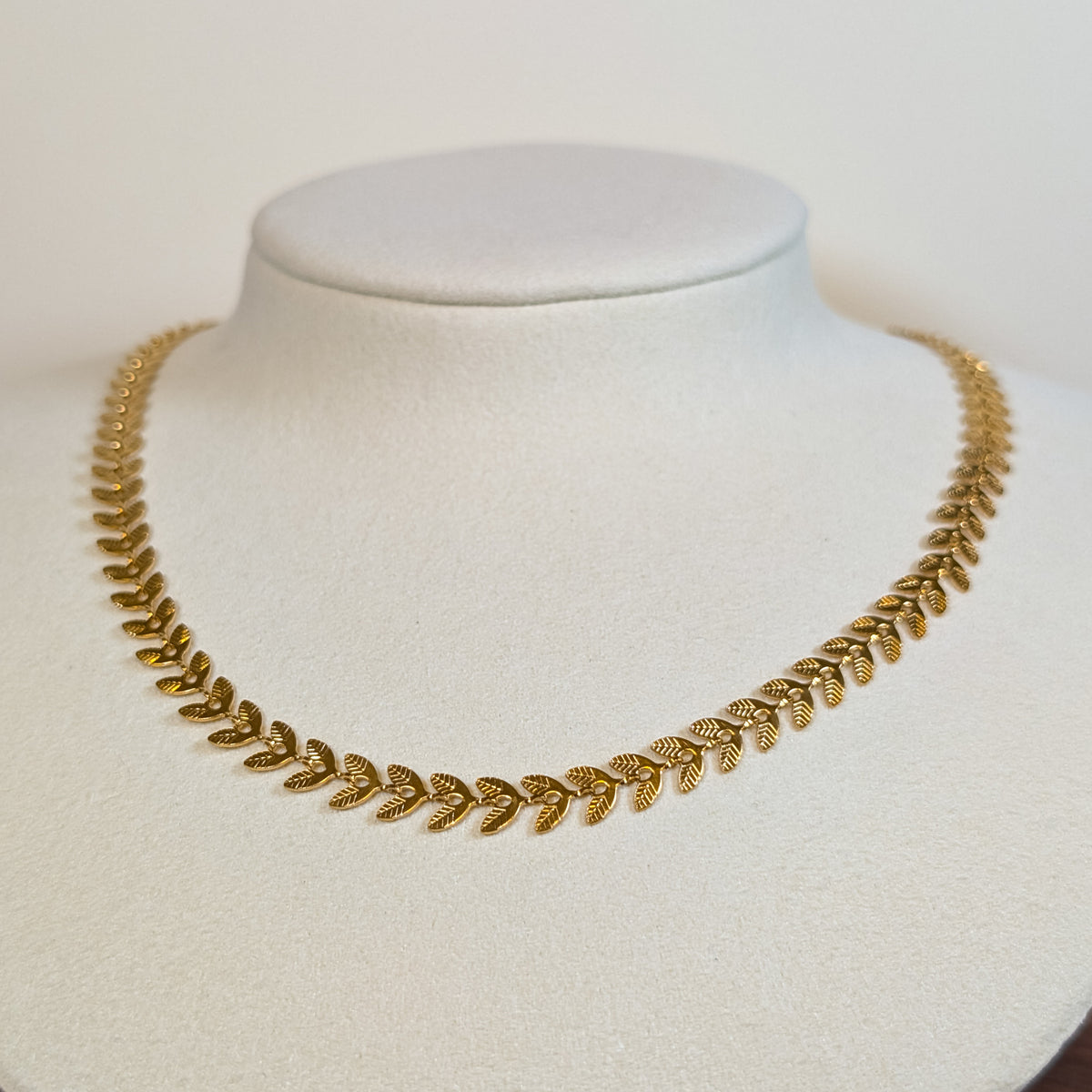 Gold-tone stainless steel choker chain woven in a laurel fishbone leaf pattern on a white display bust