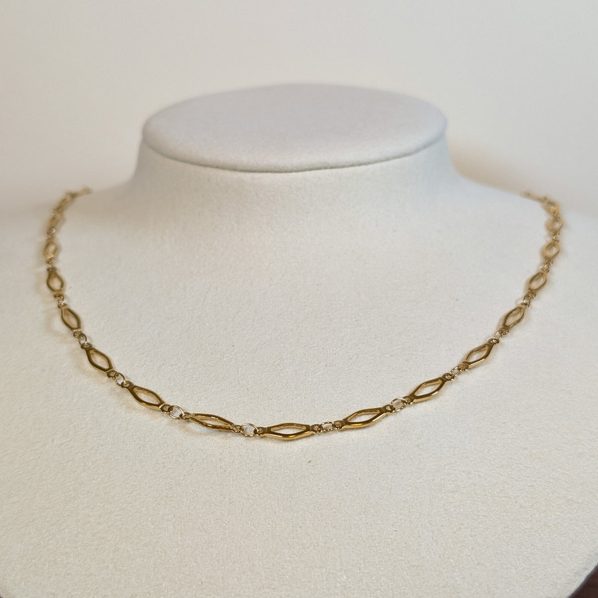 Gold-tone stainless steel choker chain of elongated marquise links on a white display bust