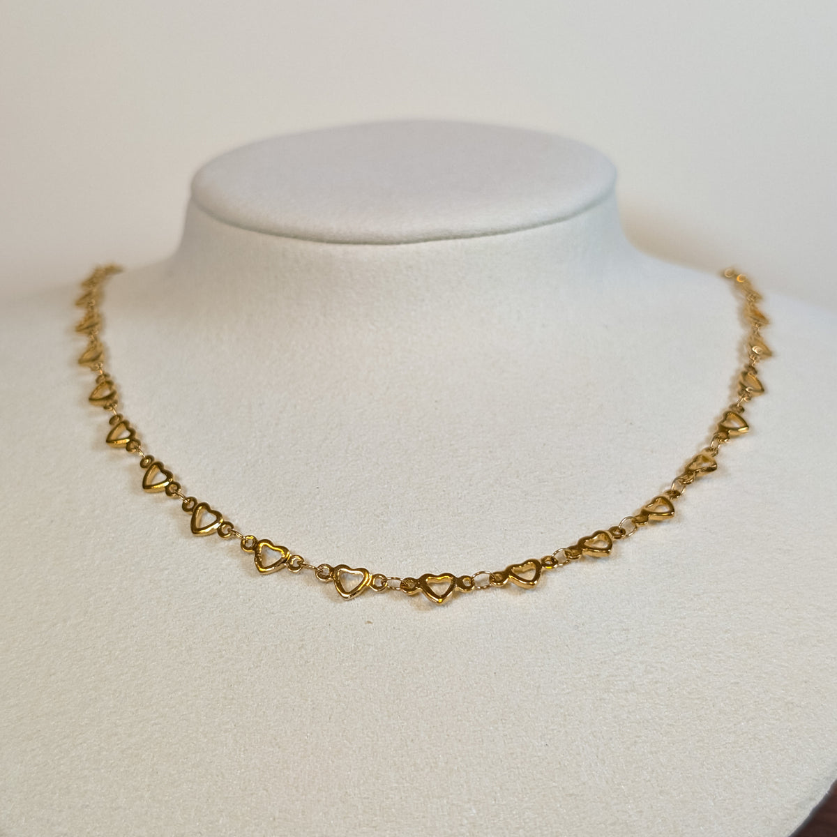 Gold-tone stainless steel choker chain of open heart links on a white display bust