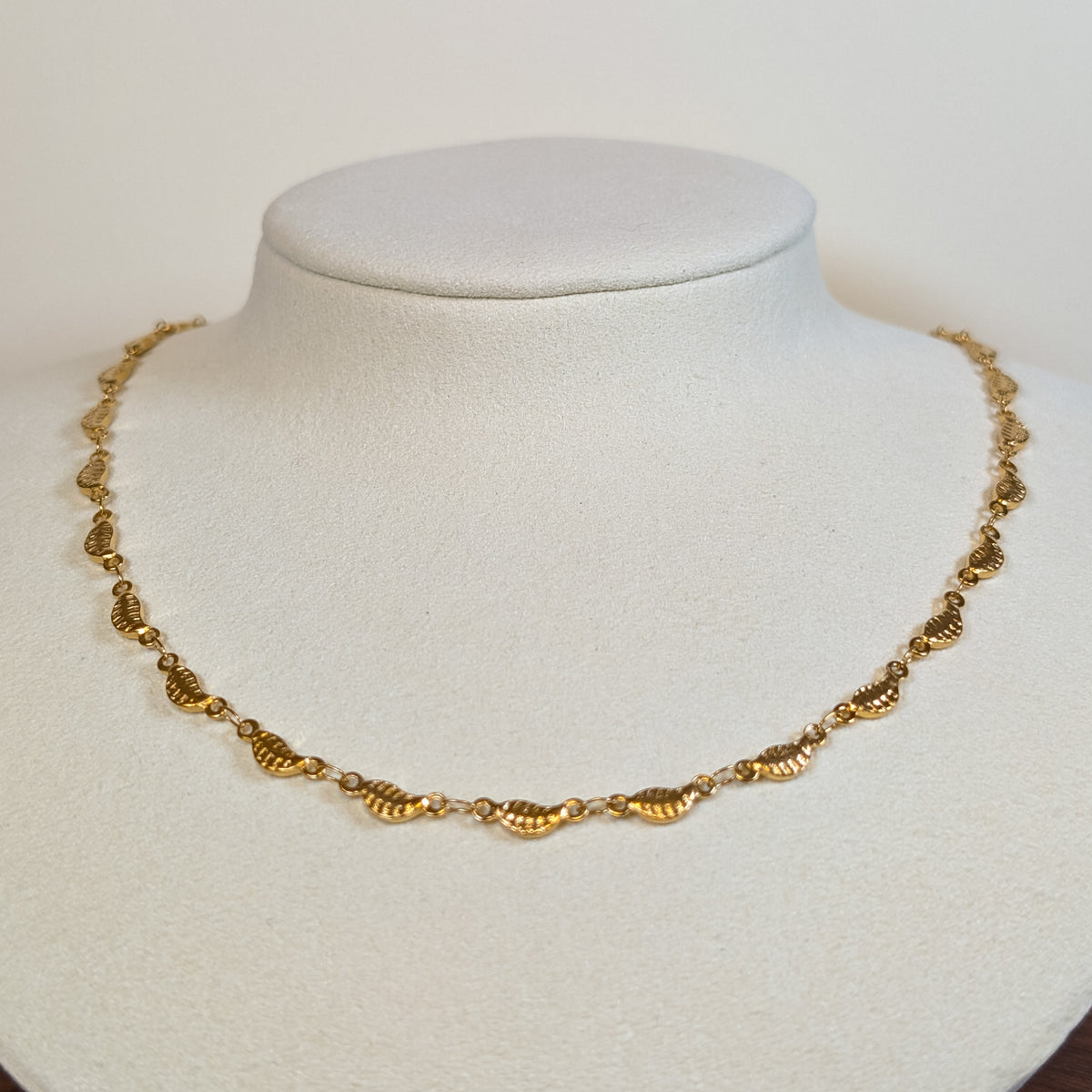 Gold-tone stainless steel choker chain of ribbed scallop shell links on a white display bust