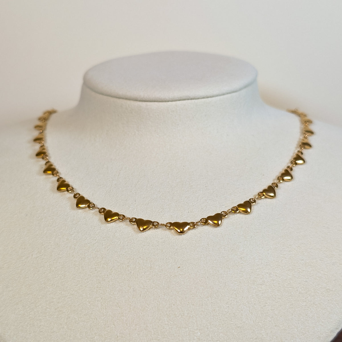 Gold-tone stainless steel choker chain of solid polished heart links on a white display bust