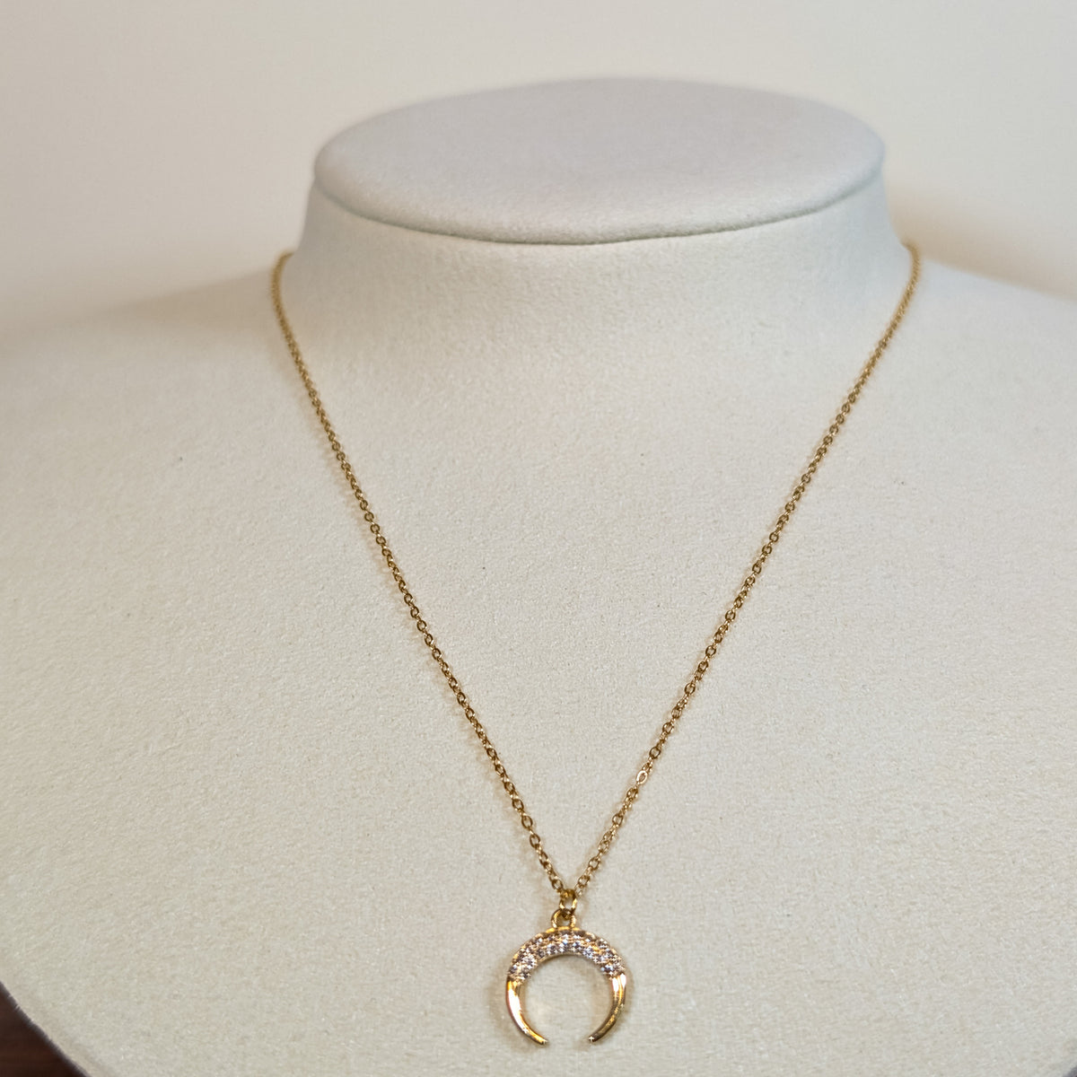 Gold-tone stainless steel necklace with a stone-set crescent horn pendant on a white display bust