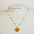 Gold-tone stainless steel necklace with a heart pendant featuring a cut-out eye and crown on a white display bust