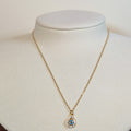 Gold-tone stainless steel necklace with a teardrop evil eye pendant in blue and clear stones on a white display bust