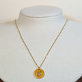 Gold-tone stainless steel necklace with a round medallion pendant with a cut-out eye on a white display bust