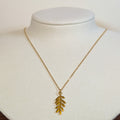 Gold-tone stainless steel necklace with a long fern leaf pendant on a white display bust