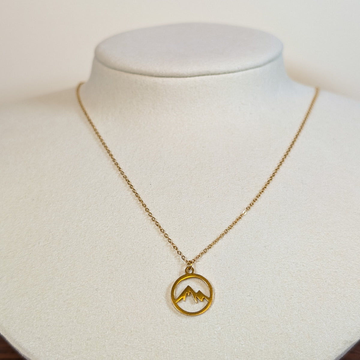 Gold-tone stainless steel necklace with a cut-out mountain range in a circle pendant on a white display bust